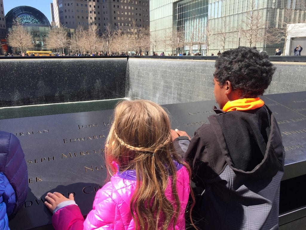 A little white girl next to a little black boy looking at the 9/11 Memorial | Global Munchkins