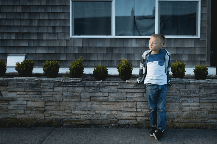 Cute boy standing in front of a Cape Cod style home | Global Munchkins photo by Kelsey Smith Photography