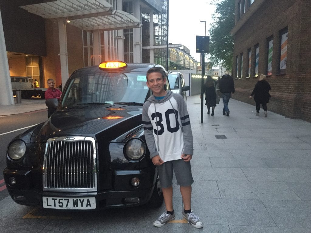 Boy standing next to a traditional London black taxi | London with Kids | Global Munchkins