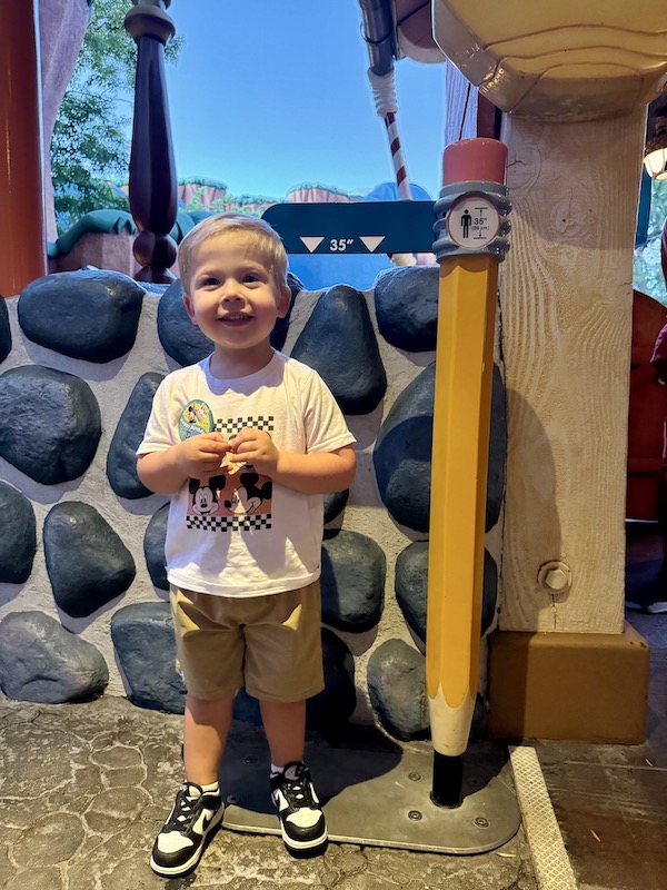 toddler at Disneyland with birthday button standing by height requirement marker