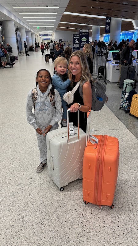 family standing in airport with 2 suitcases