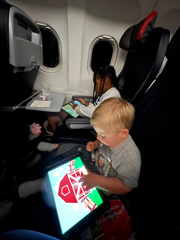 2 young kids on airplane playing on ipads